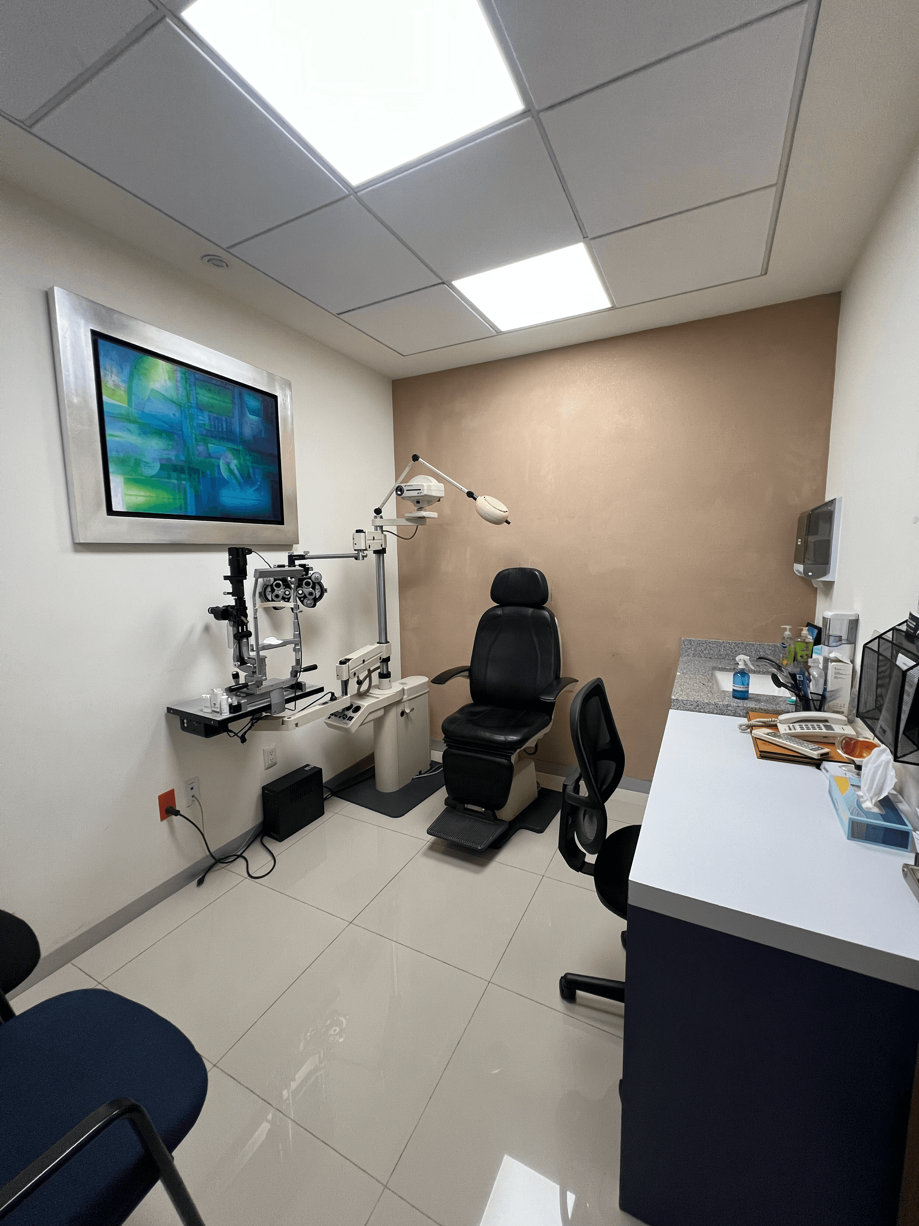 Consultorio de optometría con silla de examen negra, equipo especializado y un cuadro abstracto.